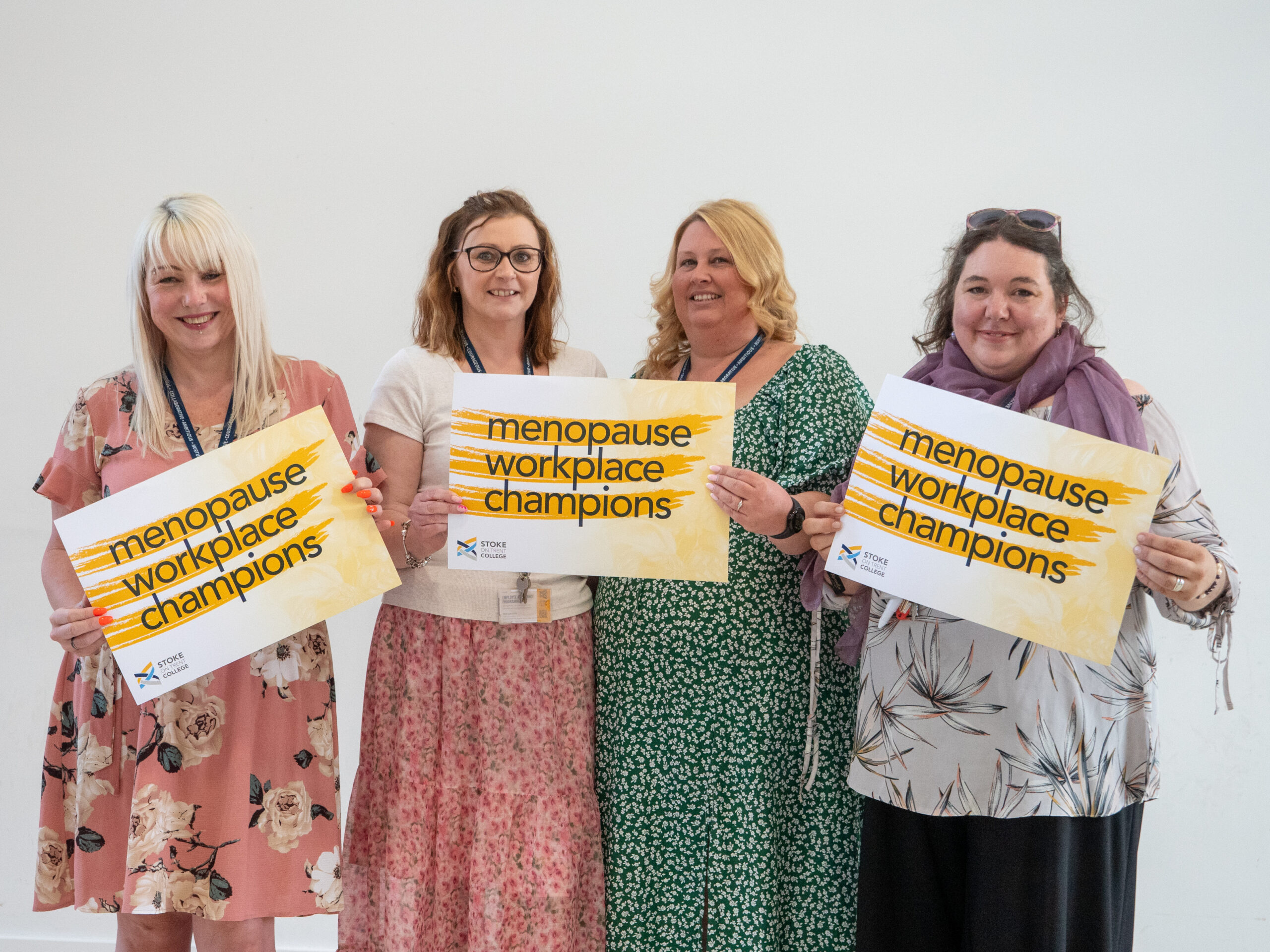 Menopause Champions at Stoke on Trent College holding signs, standing against a white wall.