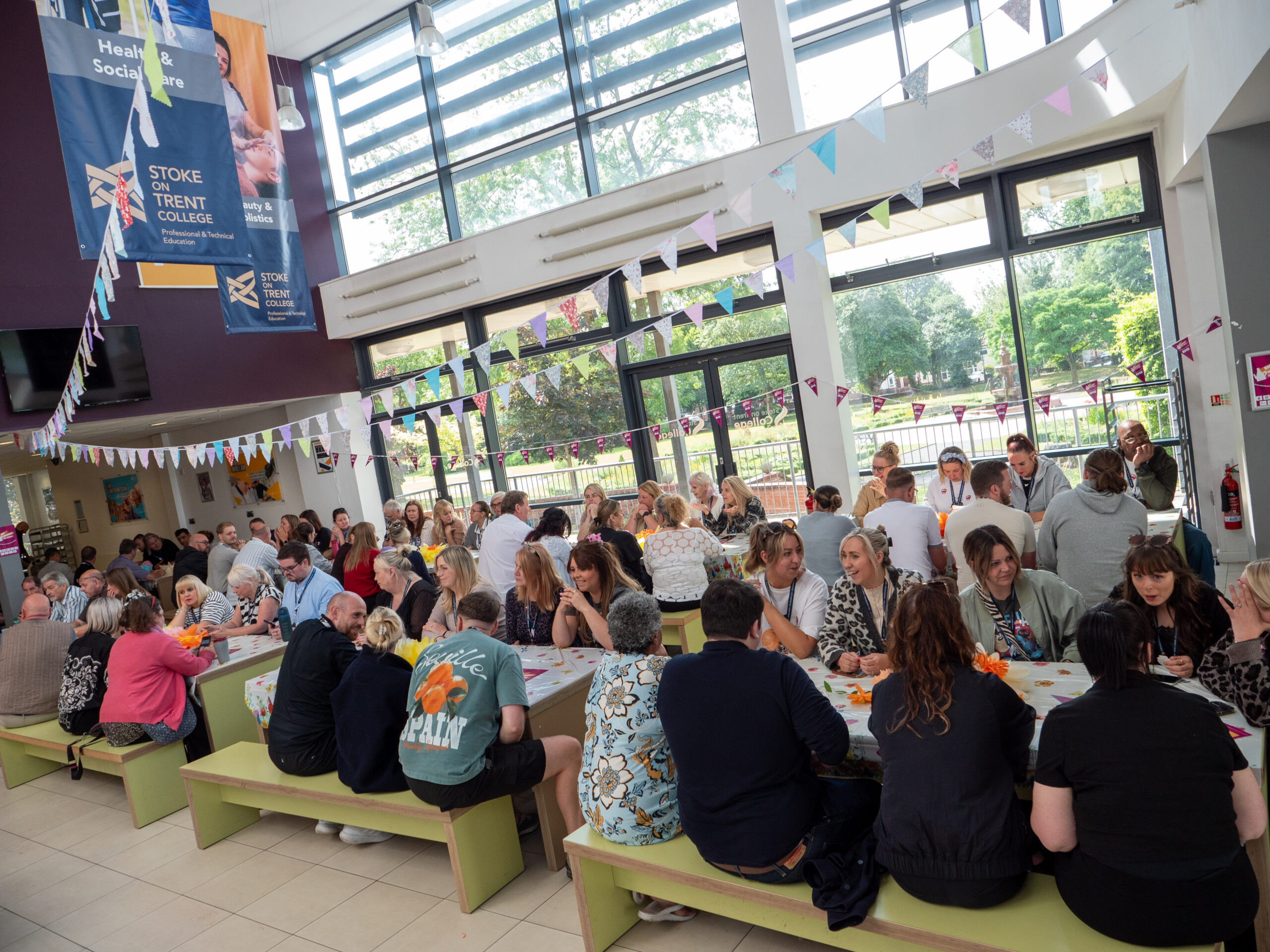 People gathered in an indoor space, sat on long tables.